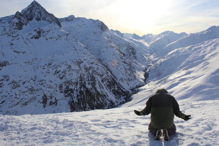 man kneeling in supplication before the sun and mountain